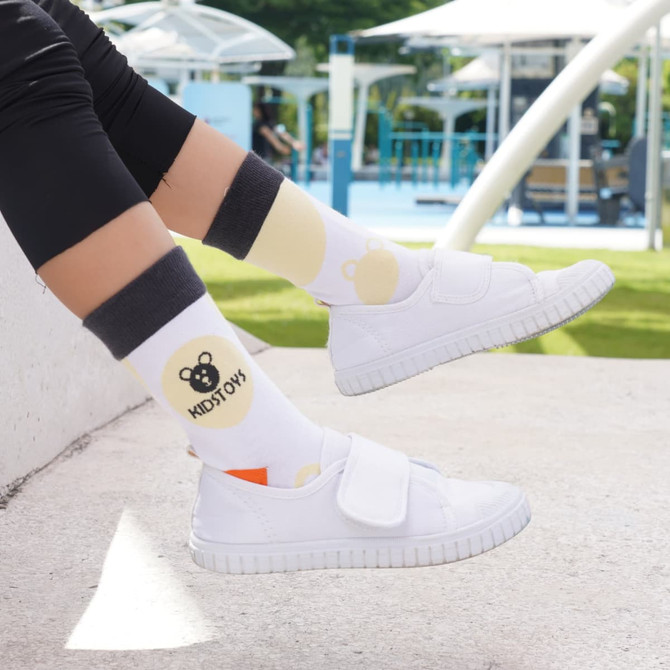 Custom patterned woven socks in white with yellow and grey designs, worn with white footwear. Features a logo.