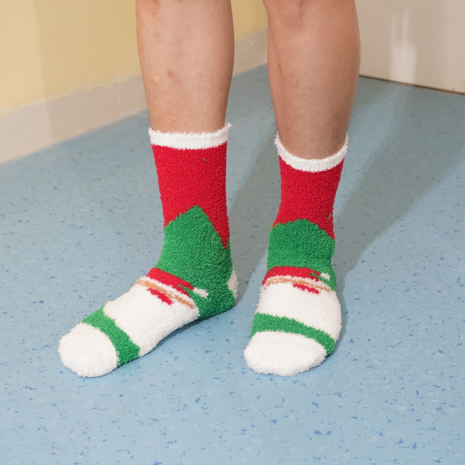 A pair of fuzzy socks featuring a red, green, and white pattern, displayed on a person's feet.