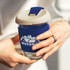 A drink bottle featuring a navy blue silicone sleeve and a natural-coloured lid, with a glass body and a logo.
