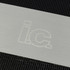 A stainless steel grill spatula is displayed on a textured black surface, featuring a subtle logo.