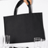 A black picnic backpack with sturdy handles, placed near glasses and tableware. It has a simple, minimalistic design.