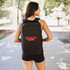 A black computer backpack with a logo, worn by a person outdoors among trees and pathways.