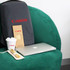 A grey backpack with a logo, a laptop, a coffee cup, and a wooden straw set on a green chair.