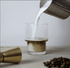 A glass tumbler with a ribbed design filled with coffee and milk, accompanied by coffee beans and a pouring jug.