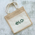 A jute tote bag featuring a natural beige and cream design, with two handles and a visible logo.