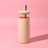 A drink bottle featuring a transparent upper section and a peachy pink outer sleeve, complete with a wooden lid and a metal straw.