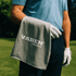 A grey golf towel with a logo, held by a person in golf attire, standing on a green golf course.