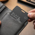 A black Bluetooth tracker being held and placed in a grey wallet pocket. The tracker features a logo.