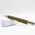A cork pen with a silver tip, resting on a white surface, featuring a green logo.