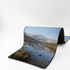 A rubber desk mat featuring a scenic landscape with mountains and a calm lake, predominantly in shades of blue and green.