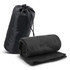 A black fleece blanket rolled and placed next to a matching carry bag, featuring a drawstring closure.
