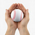 A white baseball with red stitching held between two hands. The hands are open, supporting the ball gently.