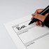 A hand holding a black marker writes on a white magnetic whiteboard with sections labelled for different topics.