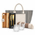 A striped tote bag with a wooden cheese board set, two glass tumblers, and a patterned blanket.
