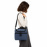 A blue cooler bag with a black adjustable strap, being carried by a person in a white sweater and grey trousers.