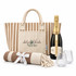 A striped tote bag, a champagne bottle, two glasses, and a blanket with a bow, all in neutral tones.