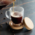 A clear glass coffee cup with a cork base and lid, featuring a stylish handle.