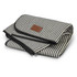 A striped picnic blanket in black and cream, neatly folded with a leather label.