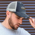 A faded navy trucker cap with a mesh back and a logo on the front, worn by a man with a beard.