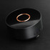 A wireless charging speaker in black with a glossy finish and a copper accent on top, featuring control buttons and a logo.