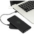 A wireless charging phone stand in black, with a smartphone on it, connected to a laptop by a charging cable.