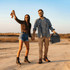 A couple holding hands outdoors, with one carrying a black lunch cooler. The scene is set against a sunset backdrop.