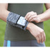 A heathered grey wristband with a pocket, holding a smartphone, worn on a person's arm against a green background.