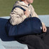 A person seated on a surface holds a large navy duffel bag with two sturdy handles. The bag has a simple design and branding.