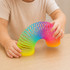 A rainbow-coloured spring toy with vibrant hues, being held by a child’s hands on a wooden surface.