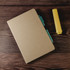 A Venture Sugarcane A5 Notebook accompanied by a blue pen and a yellow highlighter, set on a wooden background.