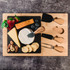 A bamboo slate cheese board featuring various cheeses, berries, nuts, and crackers, accompanied by serving utensils.