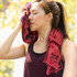 A maroon cooling towel draped around the neck of a woman, who wipes her forehead, outdoors in a sunny setting.