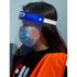 A clear full-length face shield worn by a person with a blue headband and an orange safety vest, featuring a logo.