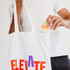 A white tote bag with colourful lettering, being held by a person as they retrieve a clear container with coloured items.