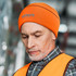 An orange, high-visibility beanie worn by a man, featuring a logo and a close-up view of his expression.