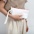 A white canvas cosmetic bag with a red zipper, held by a person wearing a striped top and light trousers.