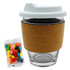A glass coffee cup with a cork band and a white lid, accompanied by a pack of colourful jelly beans.