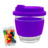 A reusable glass coffee cup with a purple silicone sleeve and lid, accompanied by a bag of colourful jelly beans.