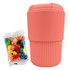 A reusable coffee cup in coral with a ribbed design, accompanied by a bag of colourful jelly beans.