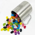 A stainless steel mug spills colourful jelly beans, including shades of yellow, pink, green, black, and white, with a carabiner.