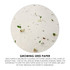 A circular close-up of seed paper showing small green sprouts emerging from a white background with black specks.