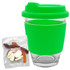 A reusable coffee cup with a bright green silicone lid and sleeve, accompanied by a packet of jelly party mix sweets.