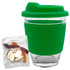 A reusable coffee cup with a clear glass body and a green silicone lid and sleeve, accompanied by a pack of jelly lollies.