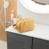 A yellow Kraft paper cosmetic bag with a zip closure, resting on a countertop. It has a handle and a logo.