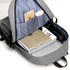 A grey laptop backpack with an open compartment displaying a laptop, magazines, and a mobile phone in pockets.