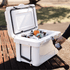 A white cooler box open with various drink bottles inside, placed on a wooden table in a park setting.