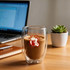 A double wall glass with a curved design, containing coffee. The glass is clear, showcasing the beverage inside.