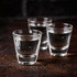 Three clear glass shot glasses with water, featuring a logo on the front.