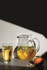 A glass highball and a pitcher filled with a light yellow drink, garnished with lime slices, against a dark background.