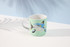 A coffee mug featuring a blue ocean creature design on a mint green background, with a handle and a logo.